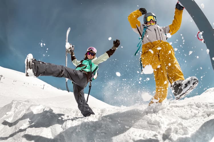 Two friends having fun and smiling in snow while holding snowboards